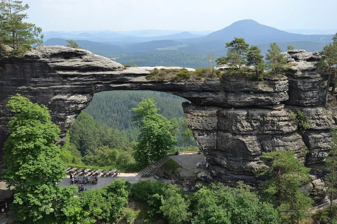 Pravčická brána, the sandstone arch in Bohemian Switzerland, with forest seen through the opening and a terrace with tables below it