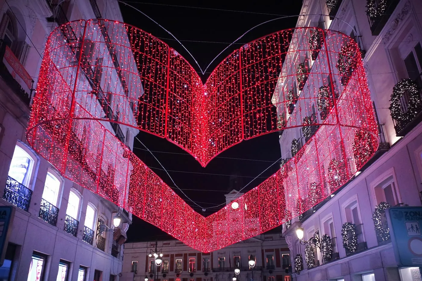 A heart of red lights strung across Calle de Preciados at night, with the clock tower on the Puerta del Sol behind