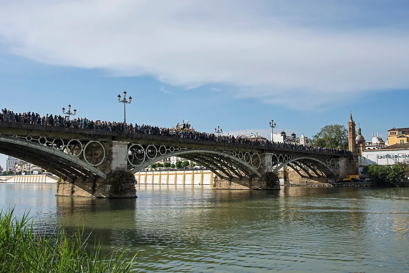 The Puente de Isabel II over the Guadalquivir with a crowd along the bridge and a church tower on the Triana bank behind