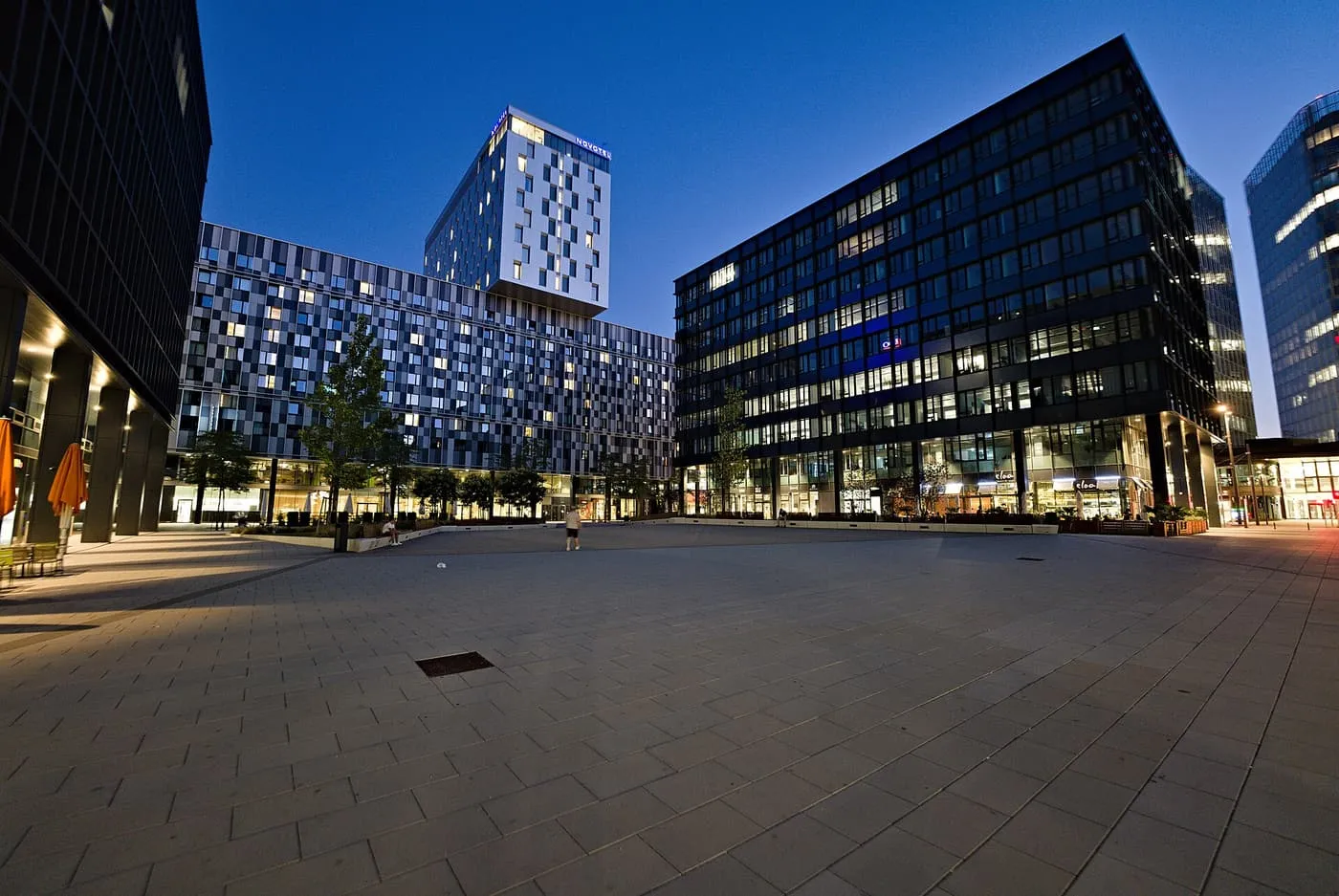 A paved square at dusk surrounded by glass and steel office and hotel blocks in Quartier Belvedere