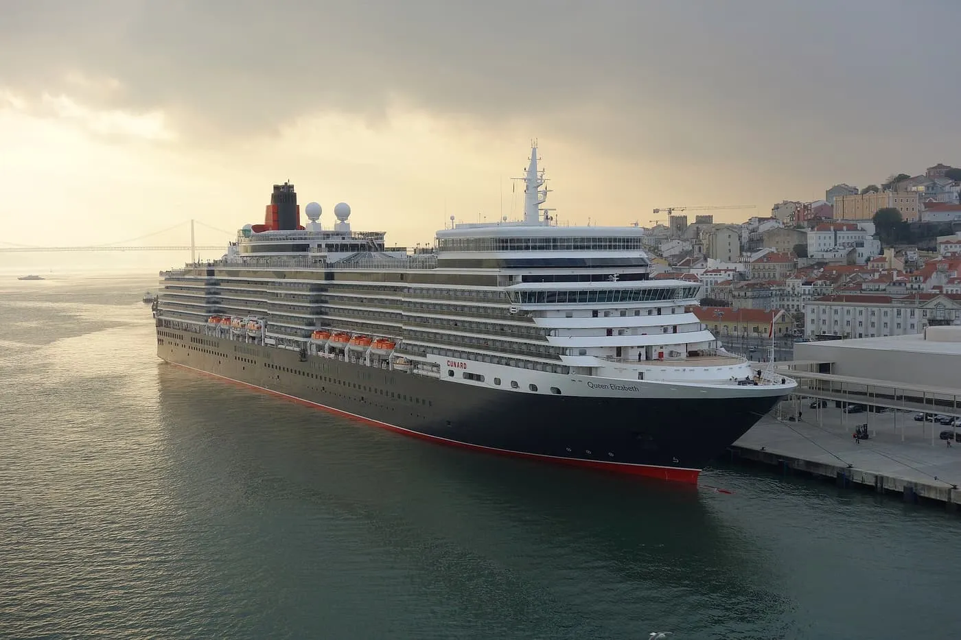 Cunard's Queen Elizabeth moored at the Lisbon cruise terminal, with the 25 de Abril Bridge on the left and Alfama's hillside on the right