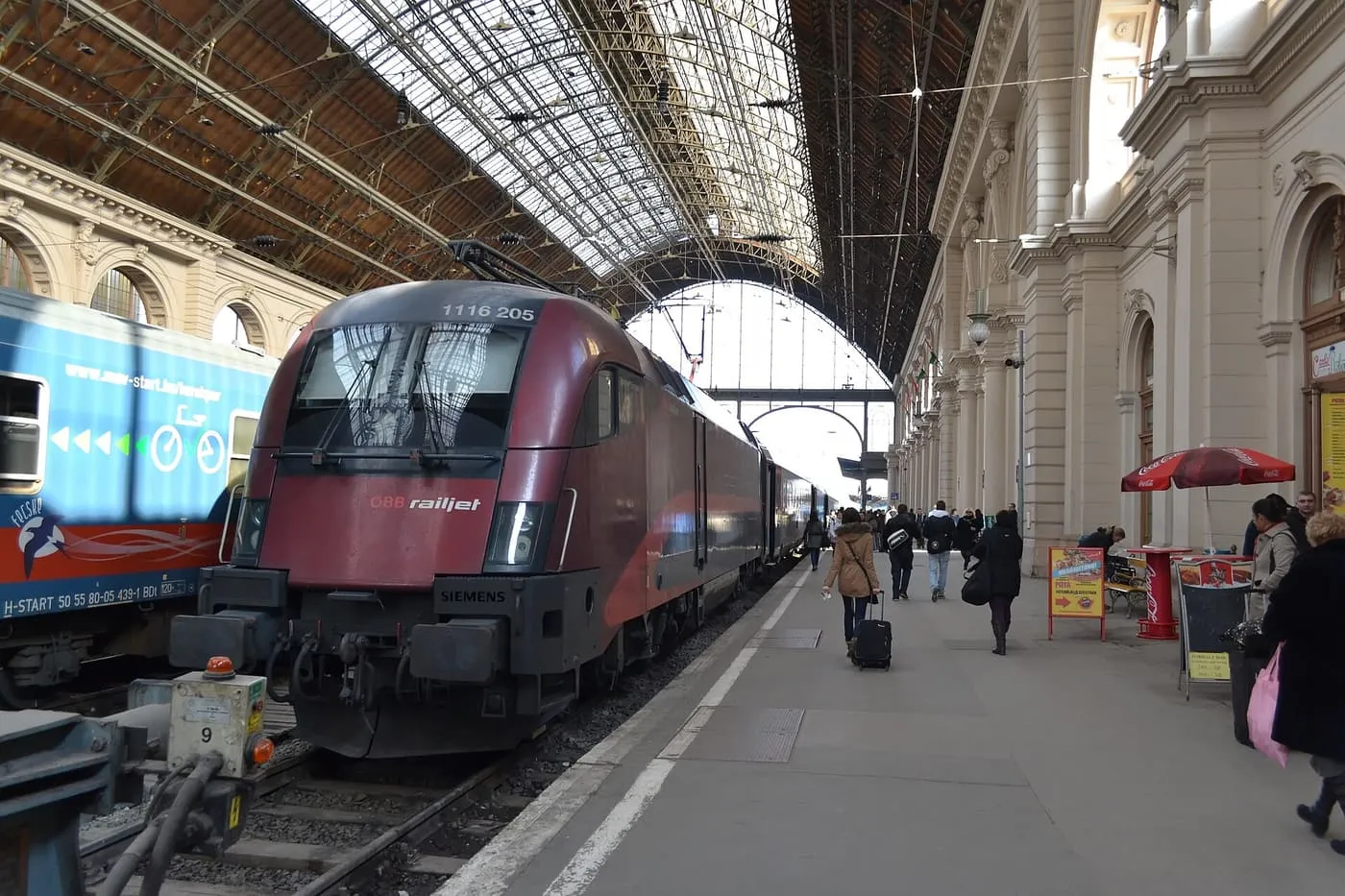 An ÖBB railjet locomotive at a platform under the glass and iron roof of Budapest Keleti station