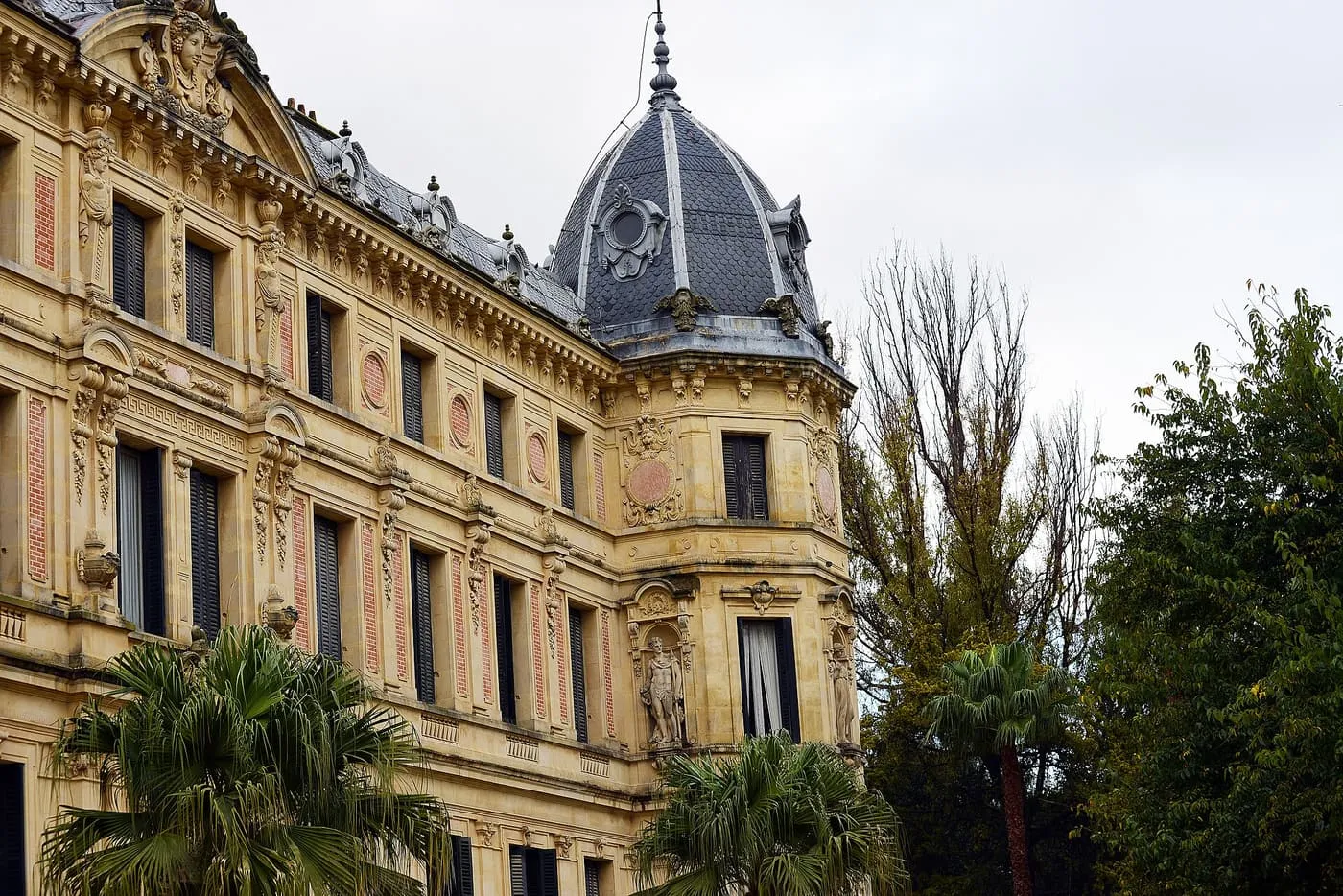 The corner tower and carved stone facade of the Recreo de las Cadenas palace in Jerez, with palm trees in front