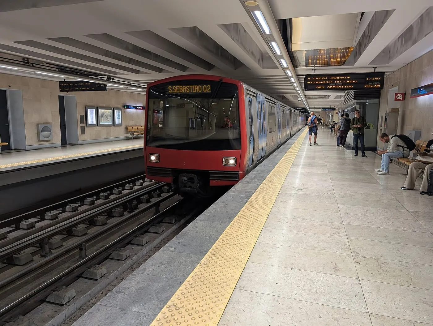 A red Metro train with São Sebastião on its destination blind standing at an Aeroporto platform