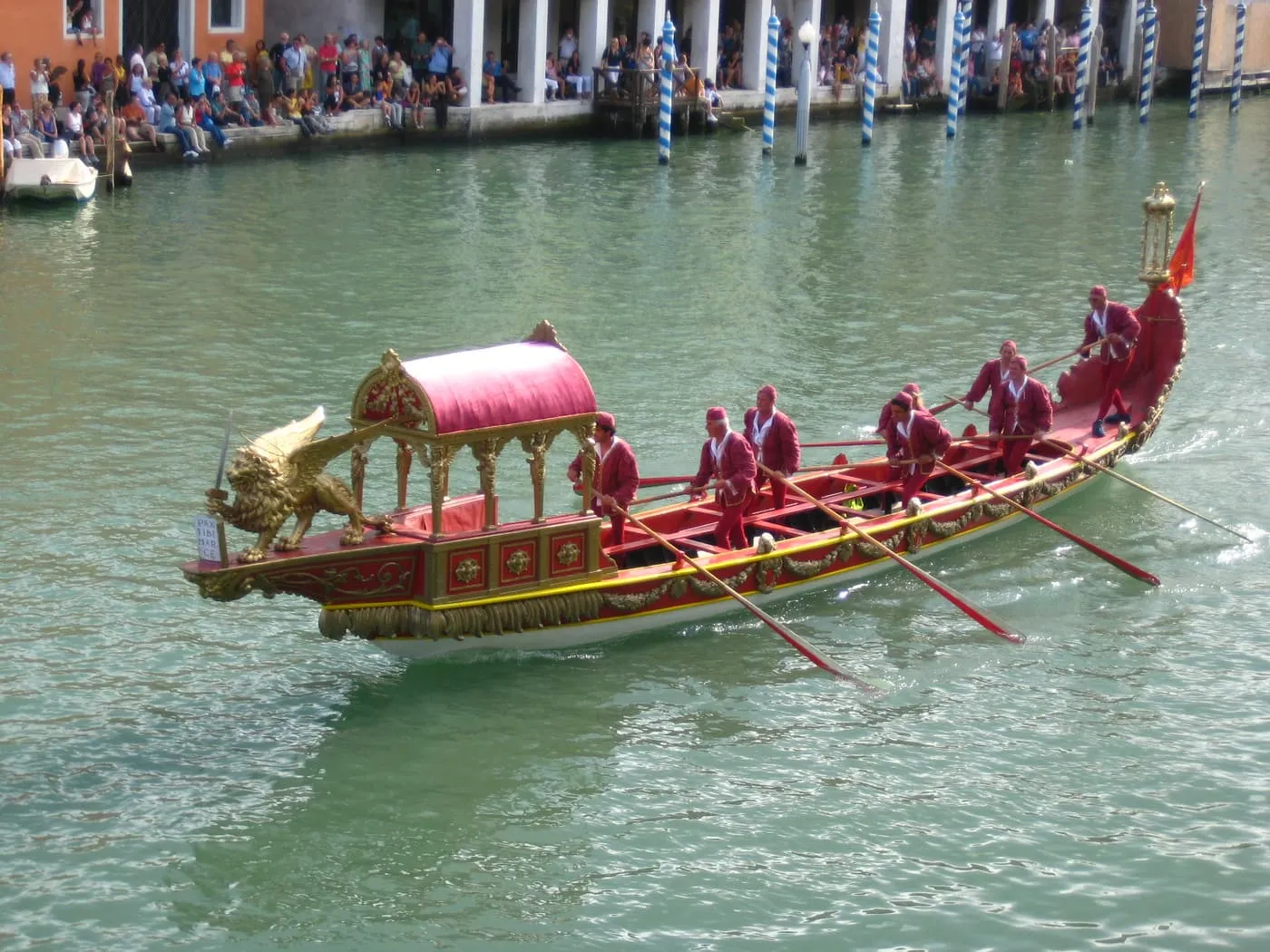 A red and gold ceremonial rowing boat with a canopy and oarsmen in red on the Grand Canal