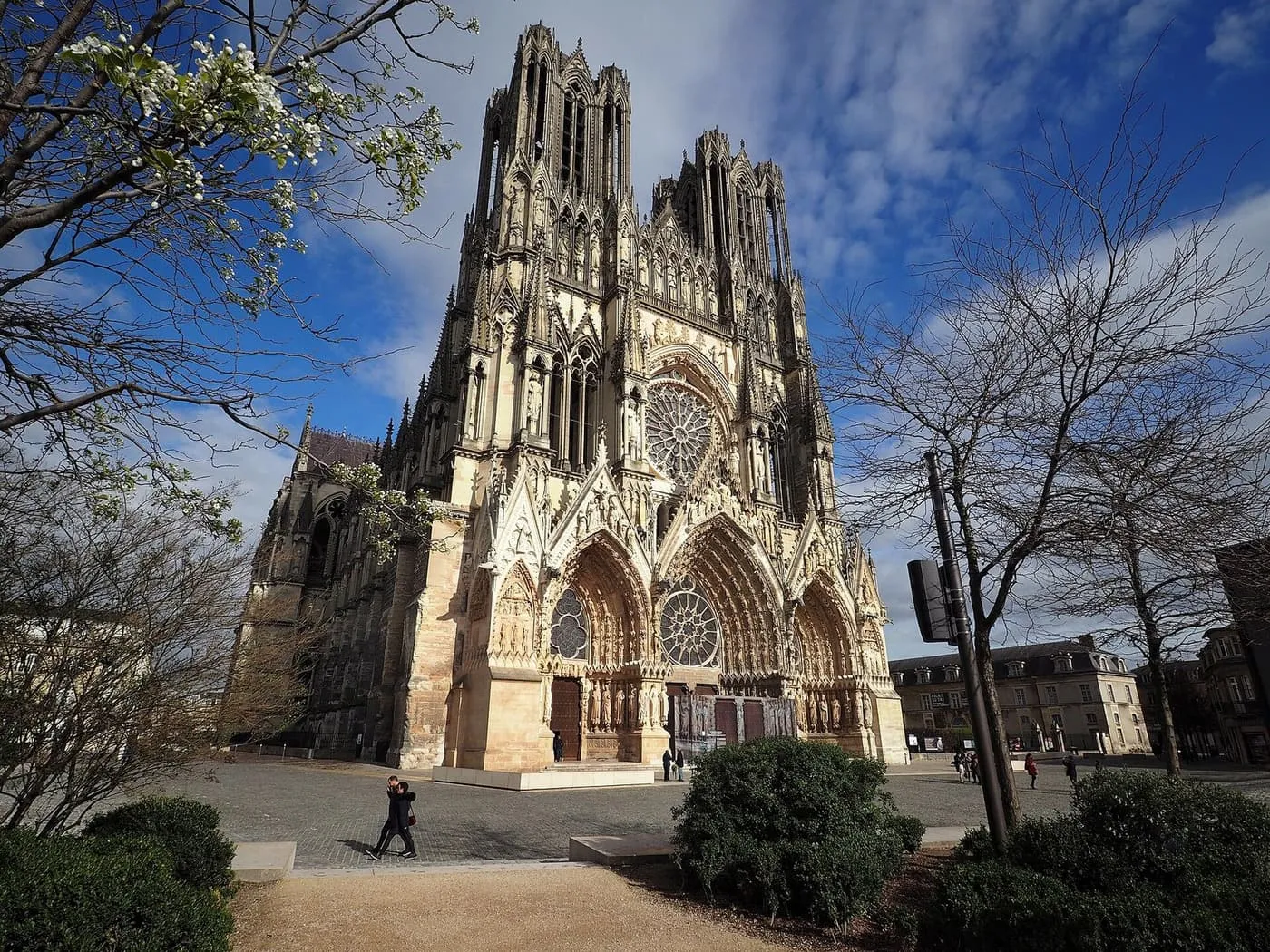 The west front of Reims Cathedral, with its rose window and three carved portals, seen across the cathedral square