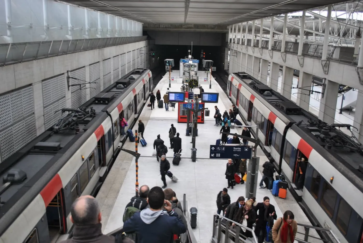 Passengers with suitcases on the RER B platforms between two trains at Aéroport Charles de Gaulle 2 TGV station