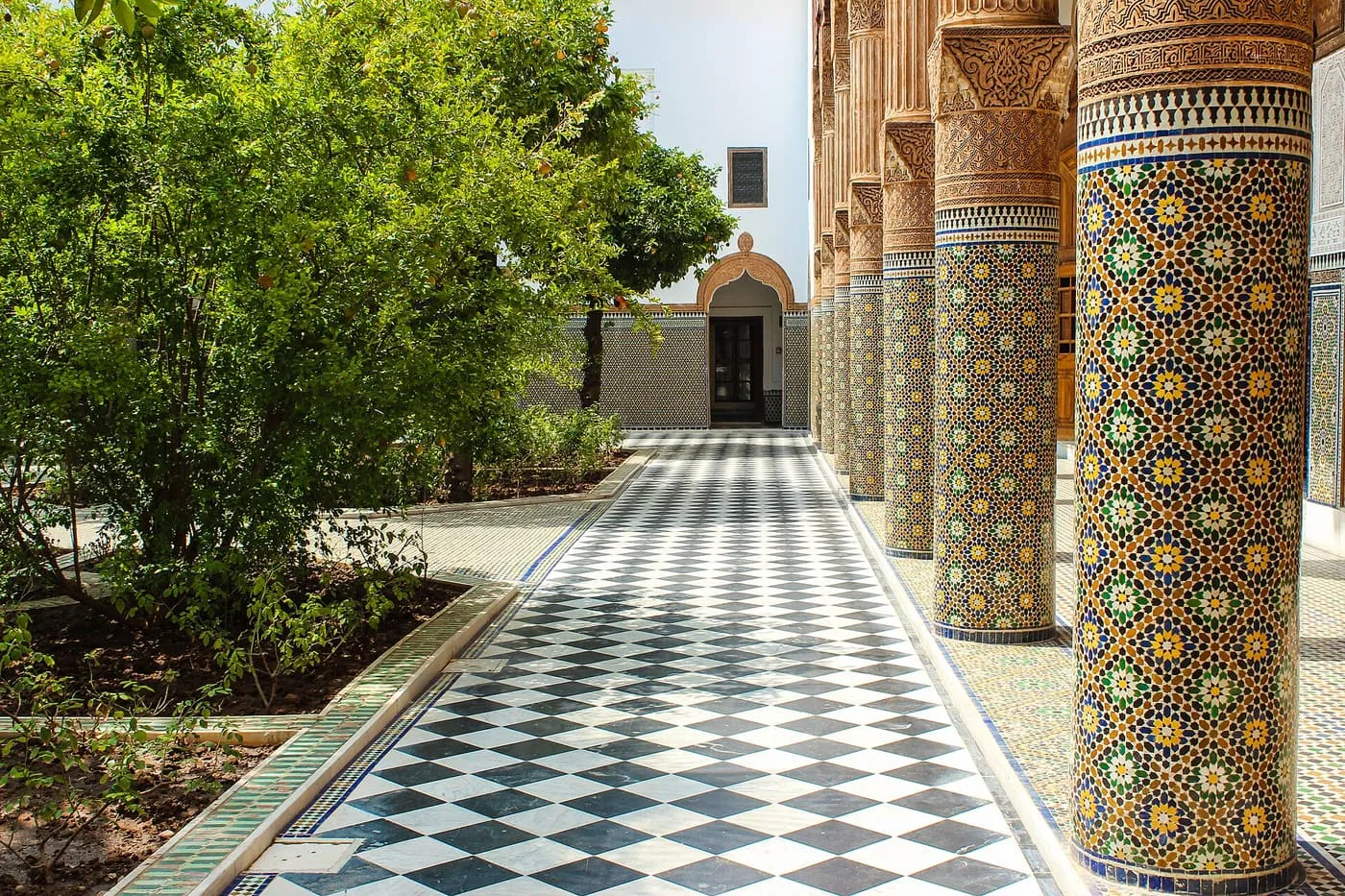 A chequerboard-tiled gallery with mosaic-tiled columns beside a courtyard of orange trees at Dar El Bacha