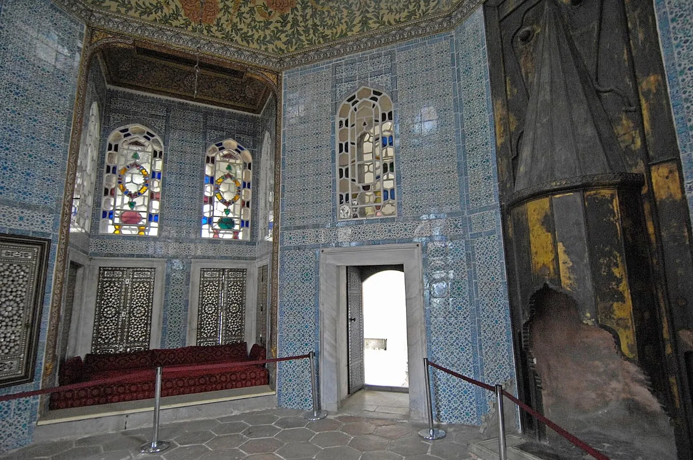 Inside the Revan Kiosk: walls covered in blue tiles, stained-glass windows, mother-of-pearl shutters and a red cushioned window seat