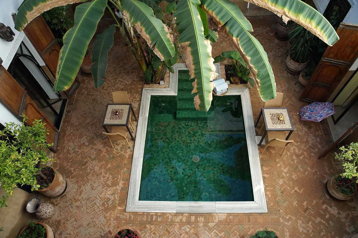 The green-tiled plunge pool in the courtyard of Riad Azzar, seen from above, with banana plants and small tables around it