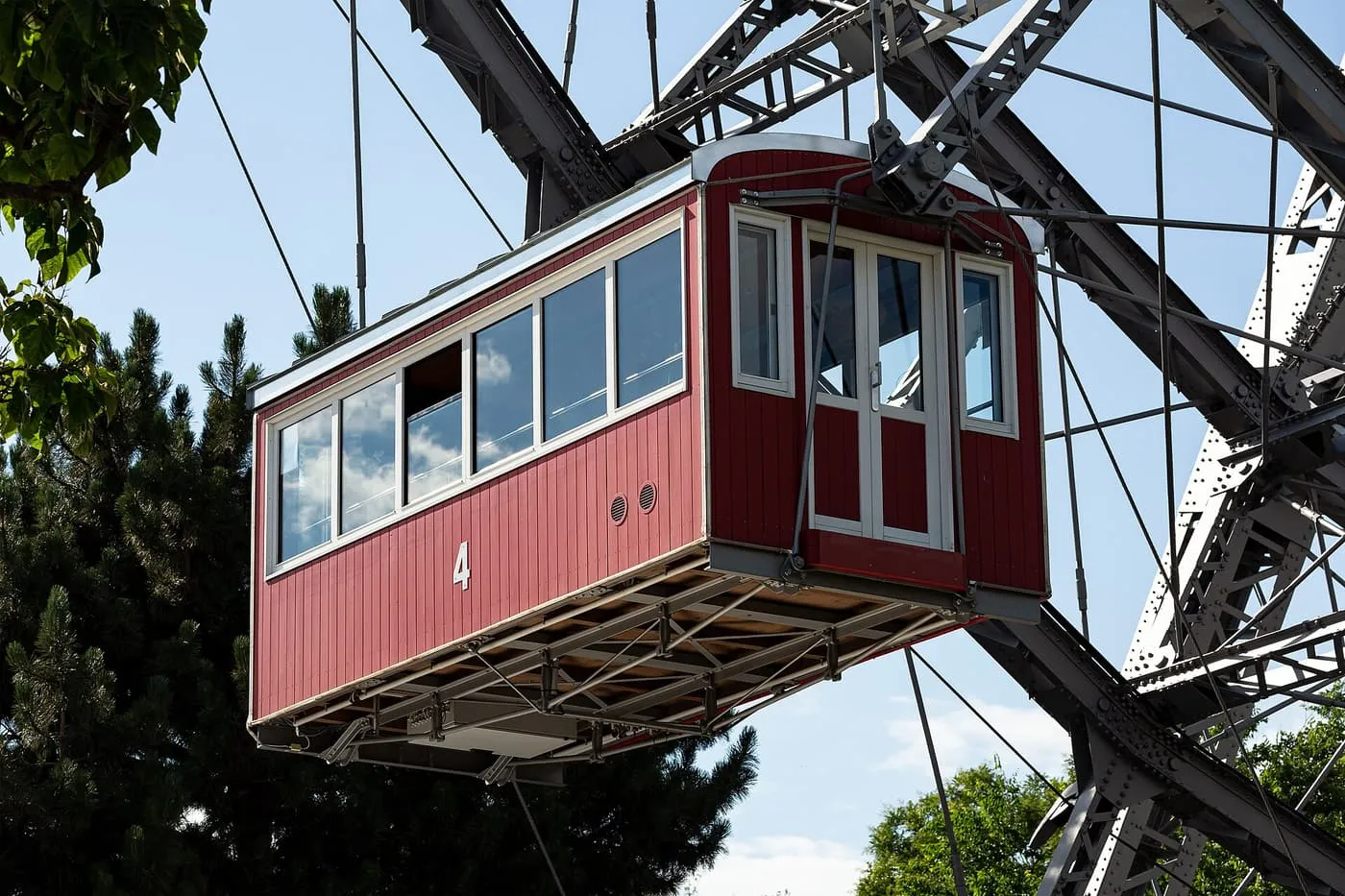 A red wooden Riesenrad cabin, number 4, hanging from the wheel's steel spokes