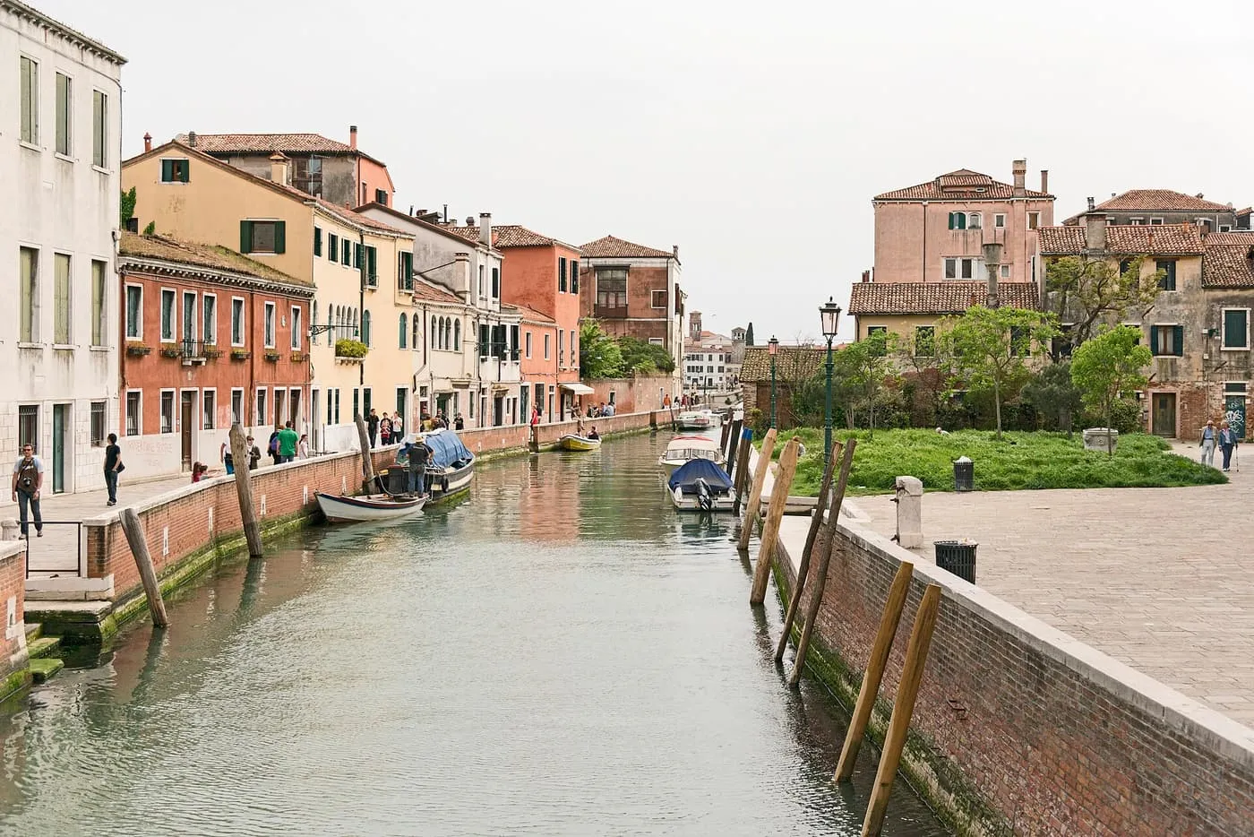 A narrow canal between pastel houses with a rowing boat moored along the left bank and a green campo on the right