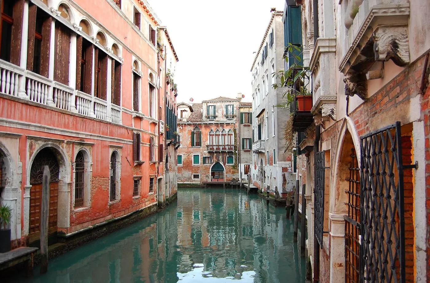 A narrow side canal between red-plastered palaces with iron-grilled doors, a palace with a water gate at the far end