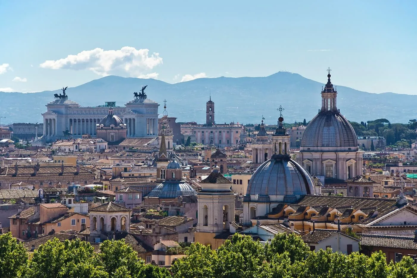 Church domes and terracotta rooftops in the centre of Rome, with the white Vittoriano monument at the left and hills behind