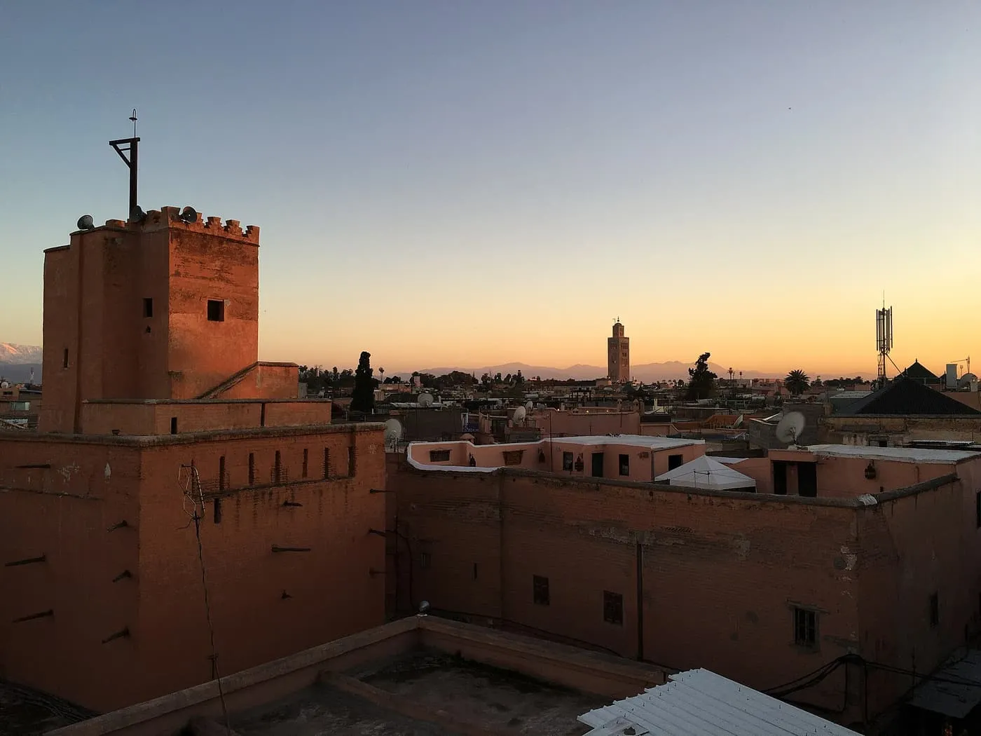Rooftops of the Mouassine quarter at dusk, with the crenellated Mouassine minaret on the left, the Koutoubia minaret on the horizon and the Atlas beyond