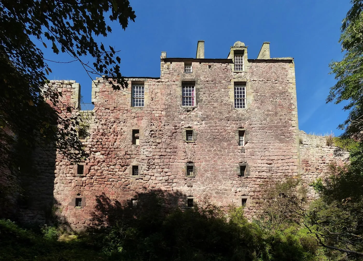 The red sandstone wall of Rosslyn Castle seen from the glen below, with trees at either side