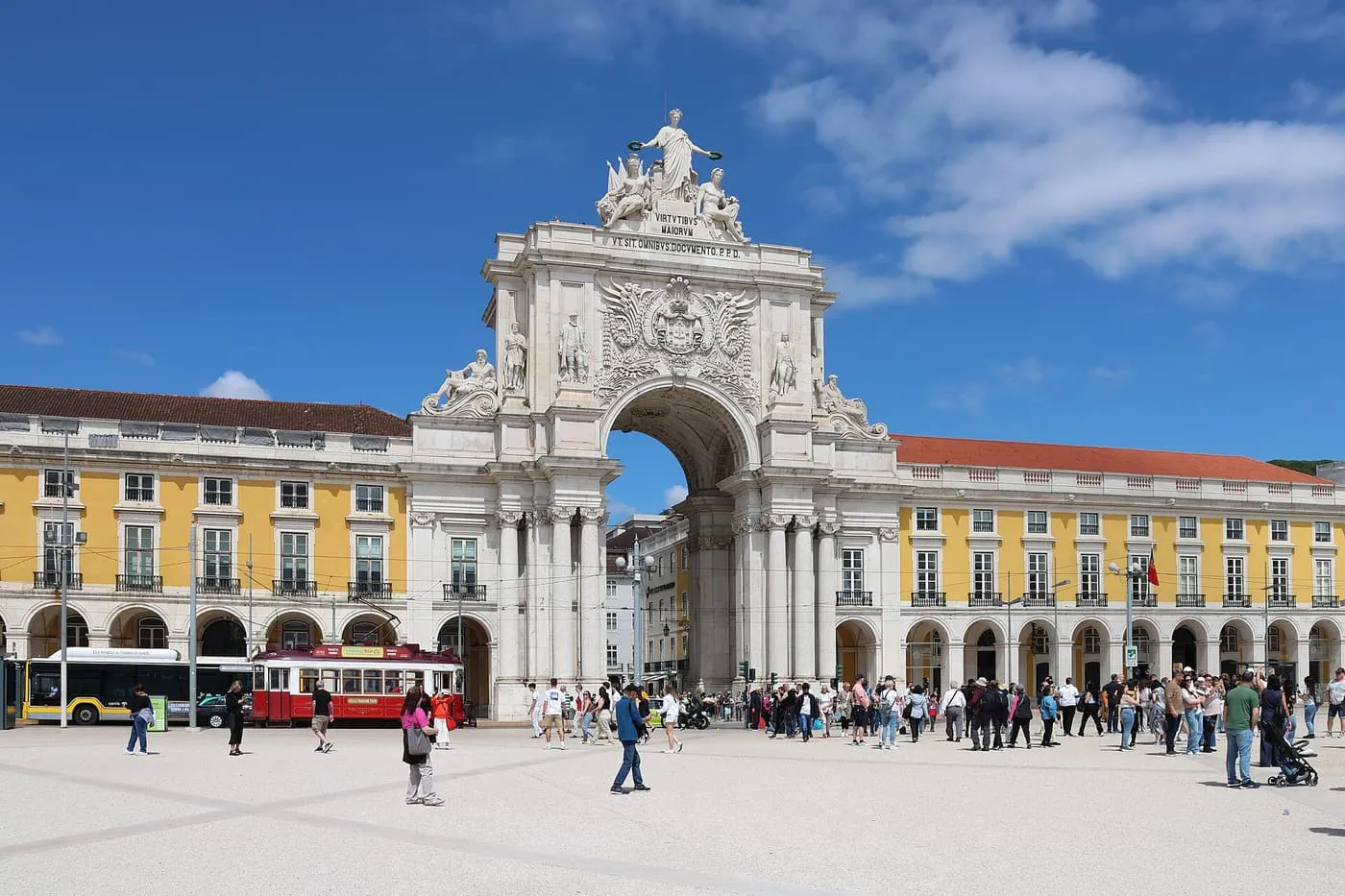 The Rua Augusta Arch on Praça do Comércio, with yellow arcades either side and a red tourist tram at its foot