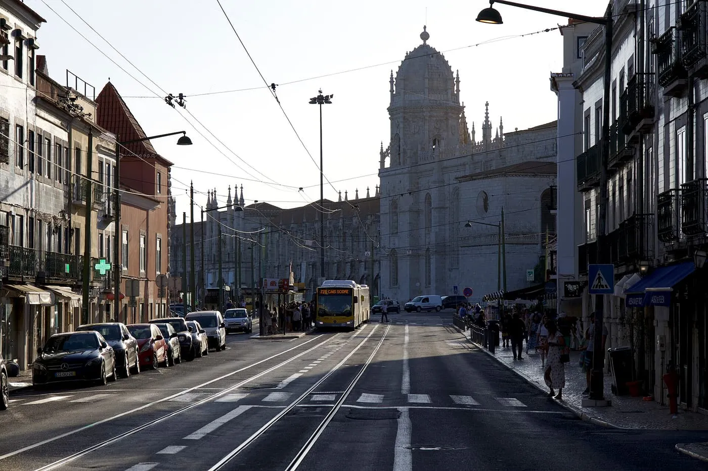 Rua de Belém in evening light, with a bus at a stop and the bell tower of the Jerónimos Monastery at the end of the street