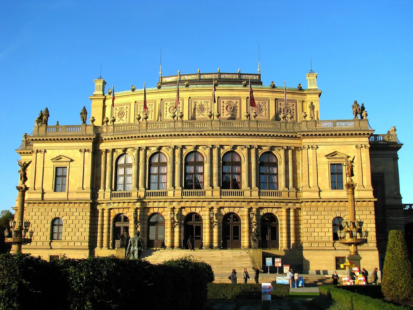 The Rudolfinum's facade in warm light, with a balustraded roofline, tall arched windows and a flight of steps in front