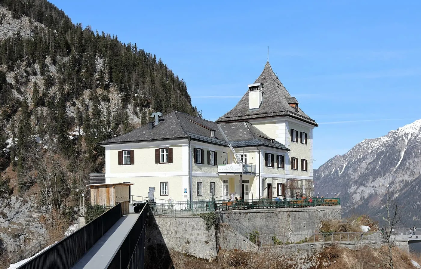 The pale yellow Rudolfsturm with its steep slate roof on the Salzberg, with snow-streaked mountains behind