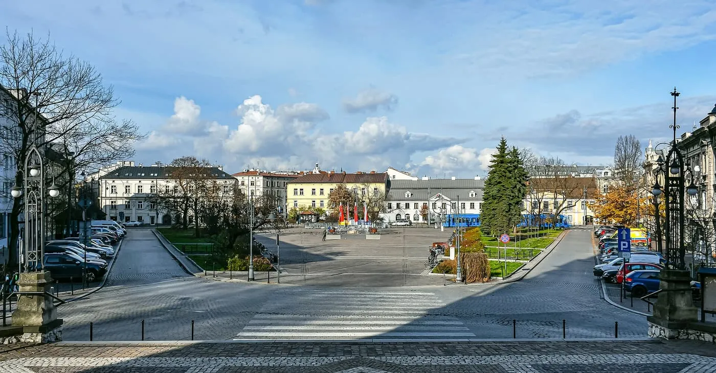 Rynek Podgórski, a wide square in Podgórze with lawns, parked cars and a tram in the distance under a blue sky