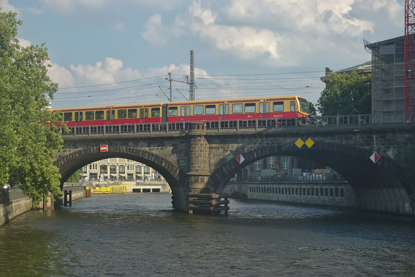 A red and yellow S-Bahn train crossing a stone arched bridge over the Spree