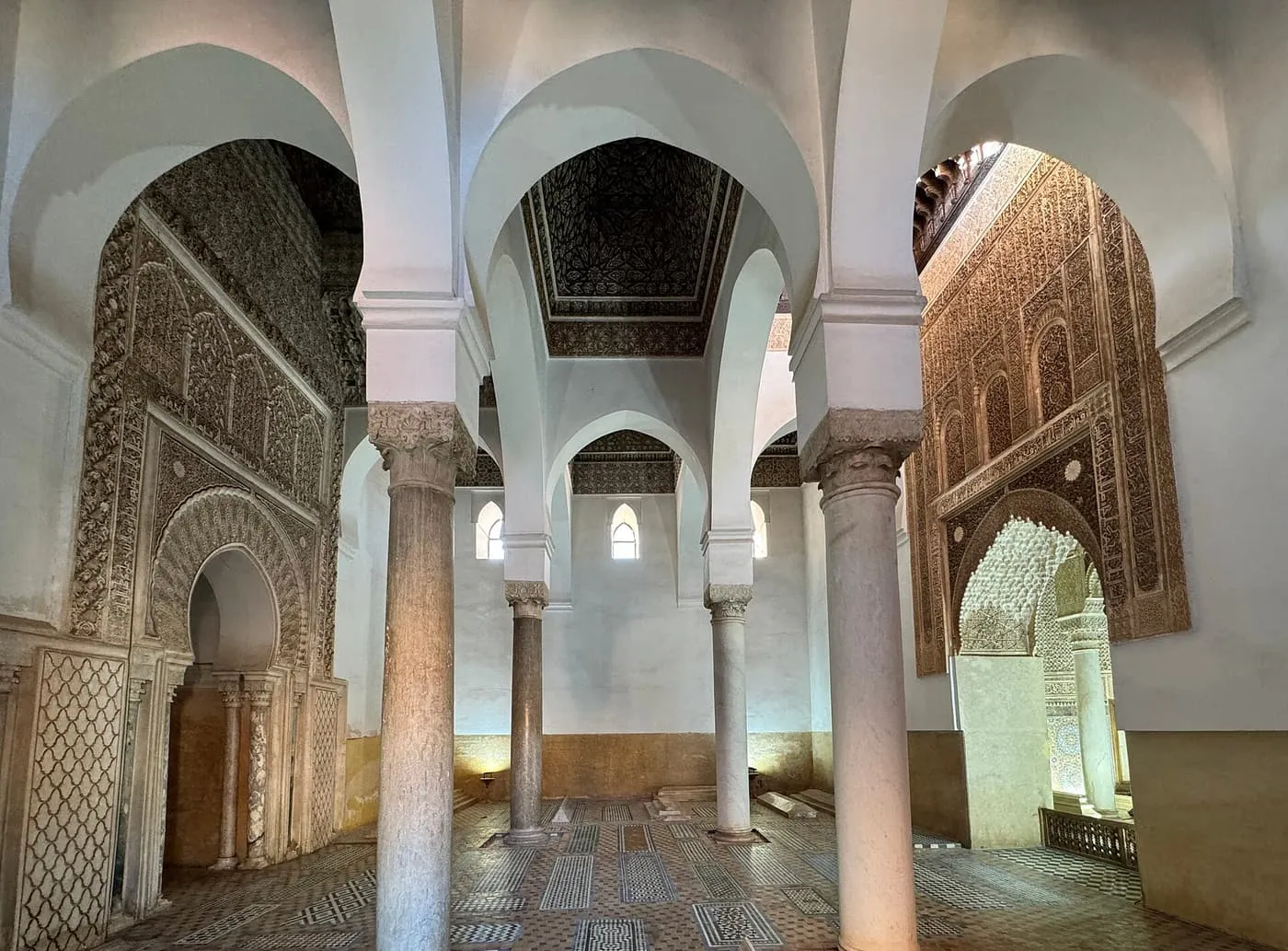 The interior of a Saadian mausoleum, with white arches on slender marble columns, carved stucco walls and a tiled floor