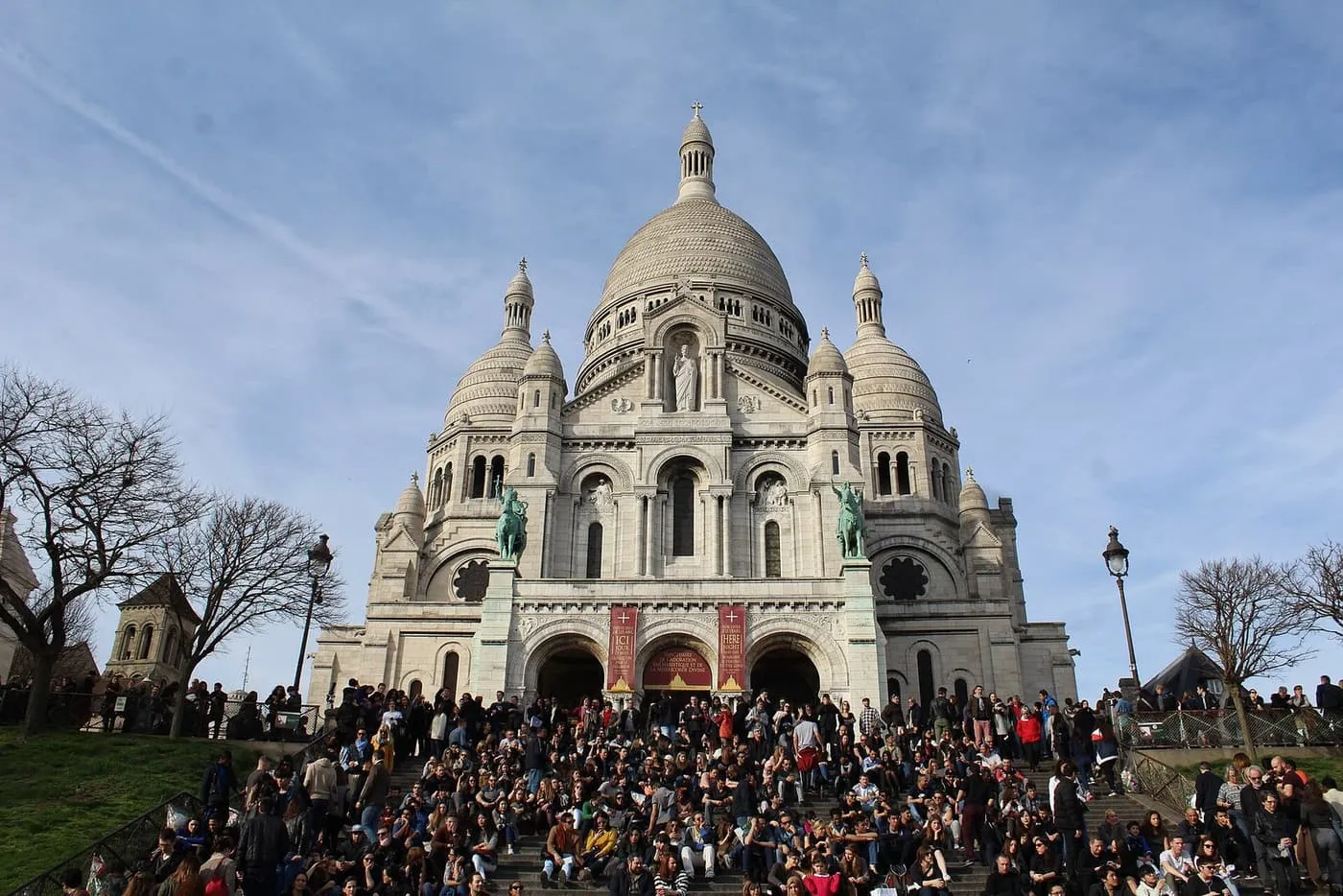 The white domes and front of the Sacré-Cœur, with visitors sitting on the steps below