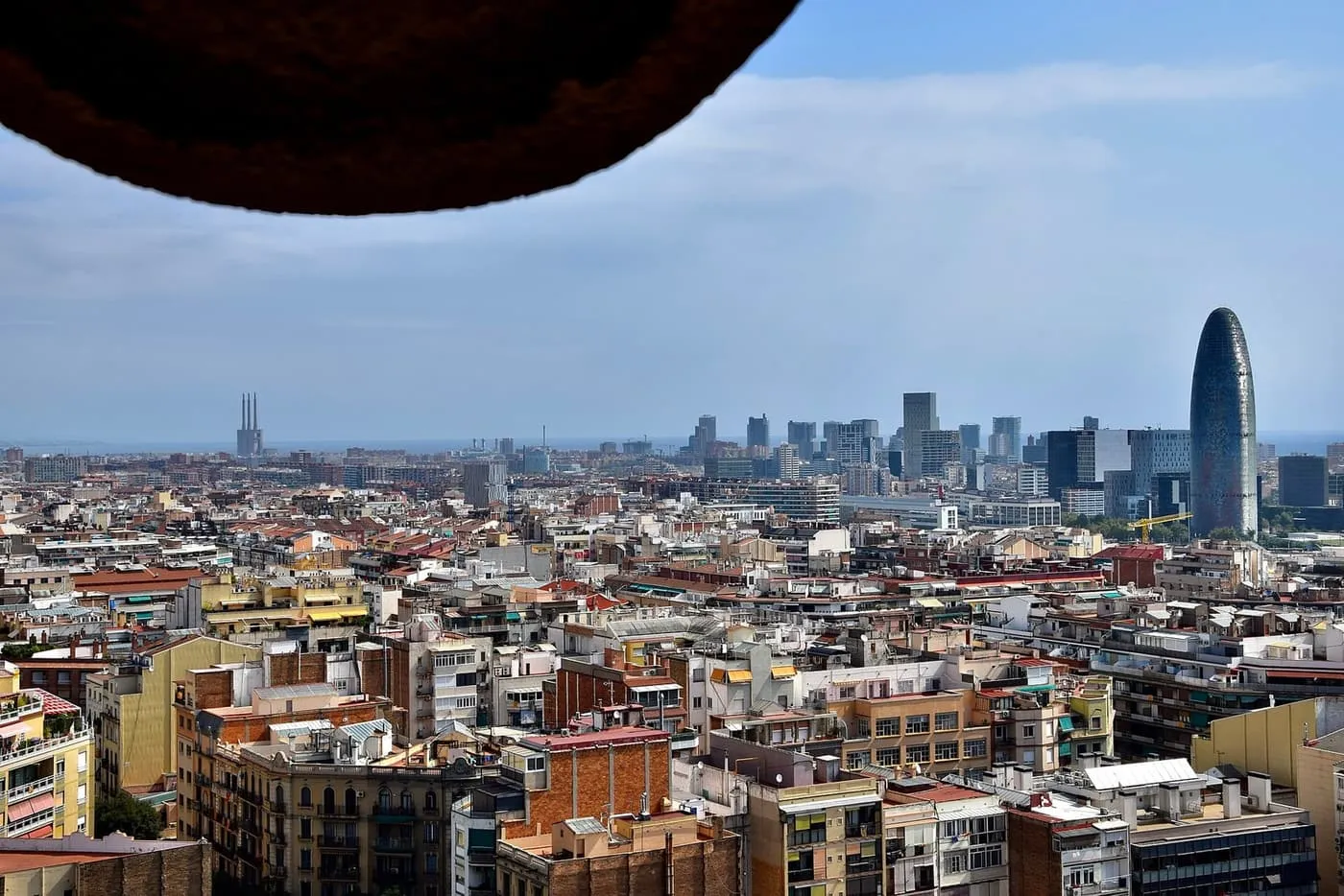 Rooftops of eastern Barcelona stretching to the sea and the Torre Glòries, framed by the stone of a Nativity tower opening