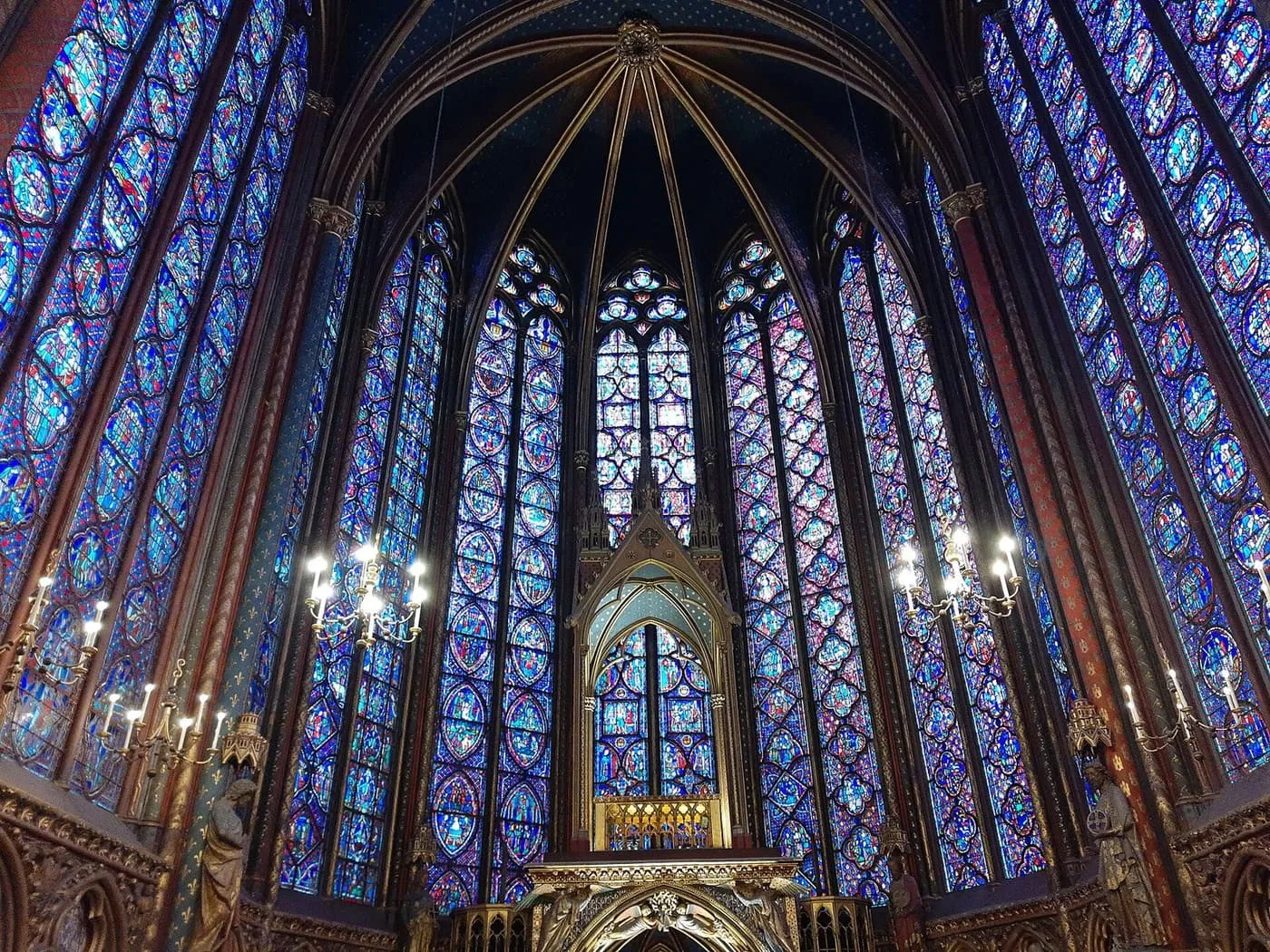 The stained-glass windows of the upper chapel of Sainte-Chapelle rising to a vaulted ceiling behind the altar