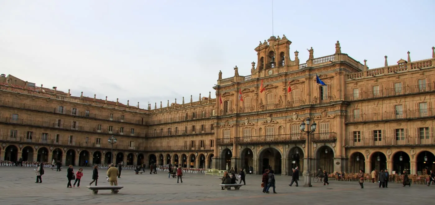 The honey-coloured stone arcades and clock tower of the town hall on Salamanca's Plaza Mayor, with people crossing the square