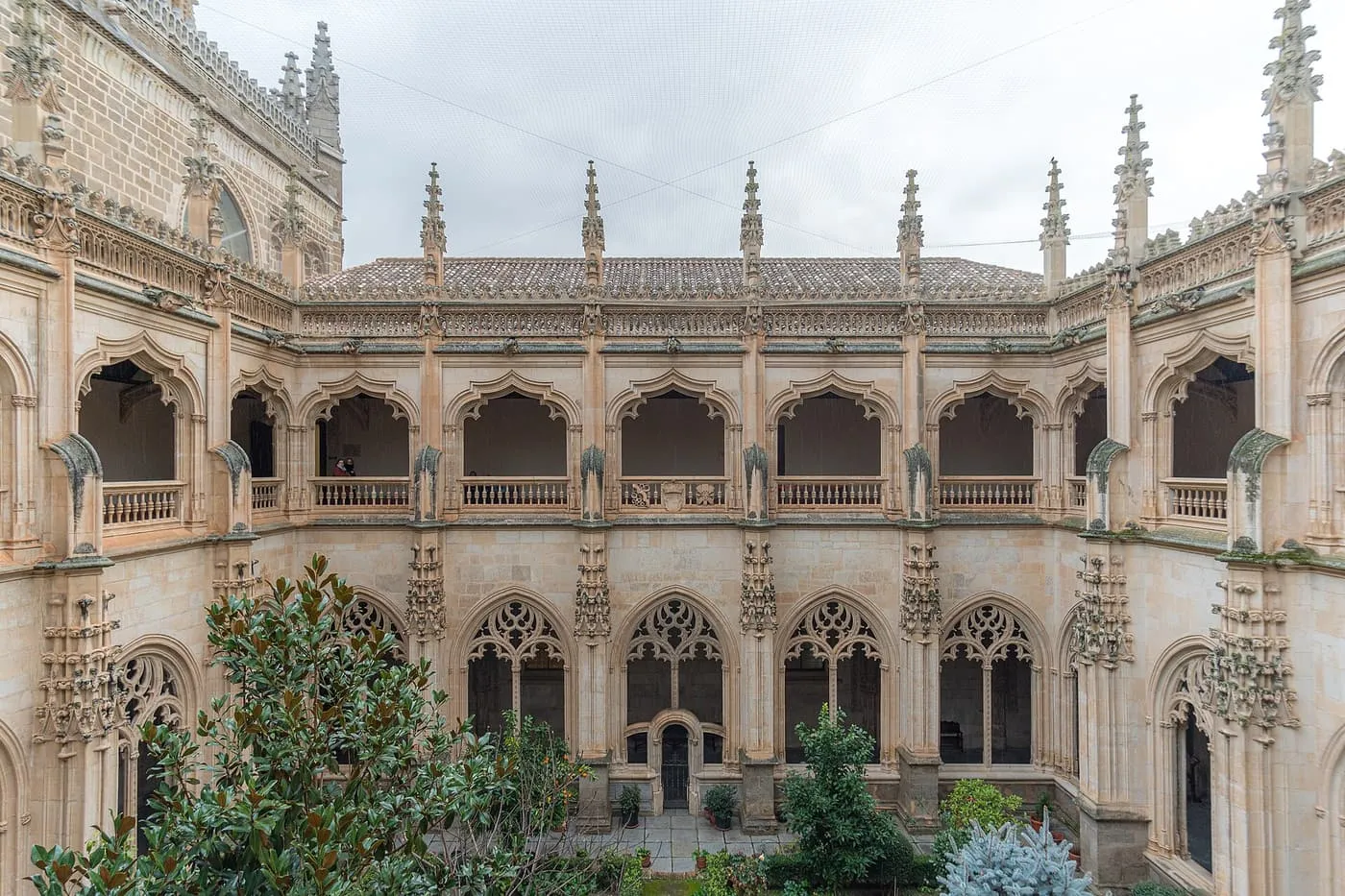 The two-storey Gothic cloister of San Juan de los Reyes seen from the upper gallery, with a magnolia and orange trees in the garden below