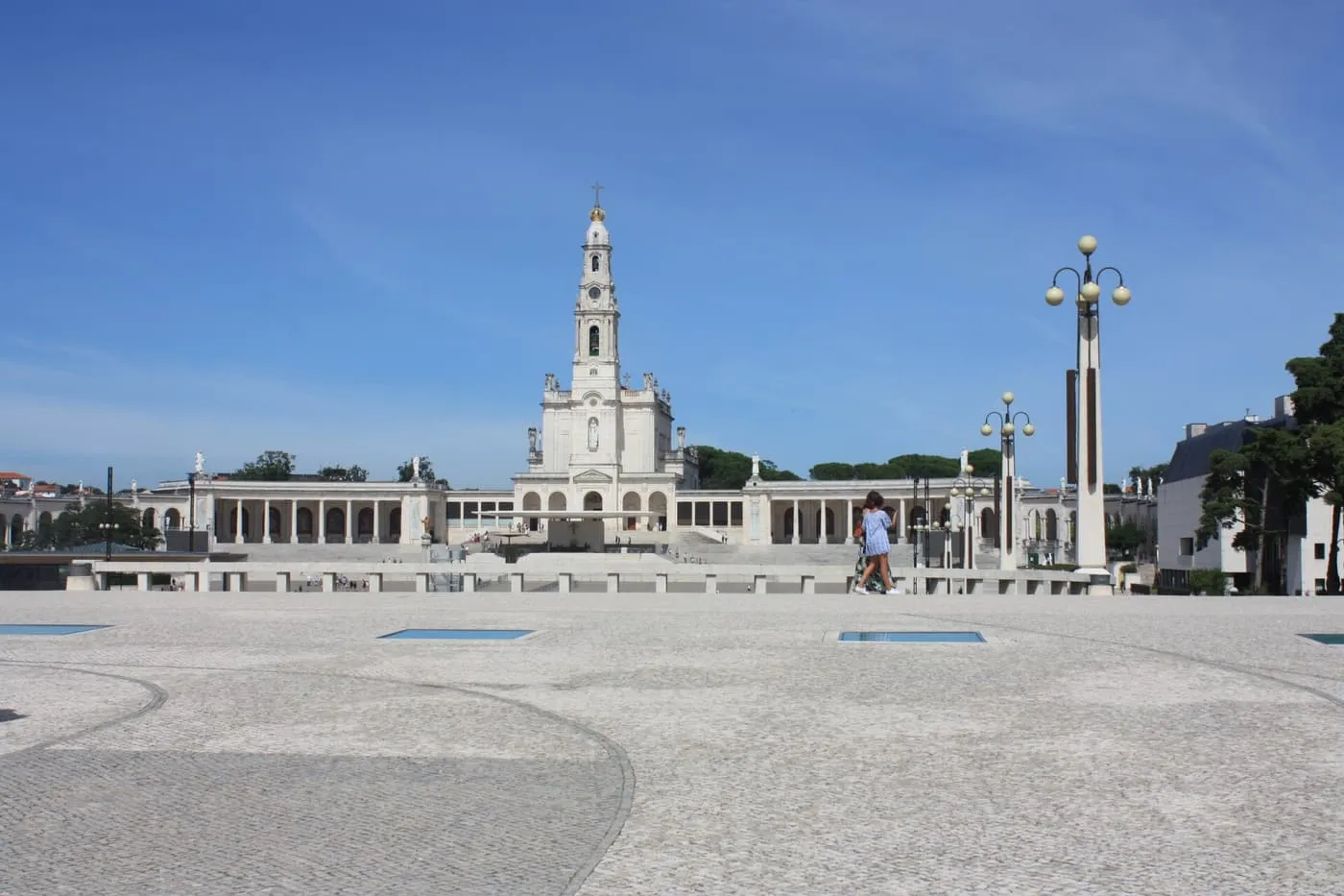 The Basilica of Our Lady of the Rosary and its tower at the far end of the wide paved square of the Sanctuary of Fátima, in daylight