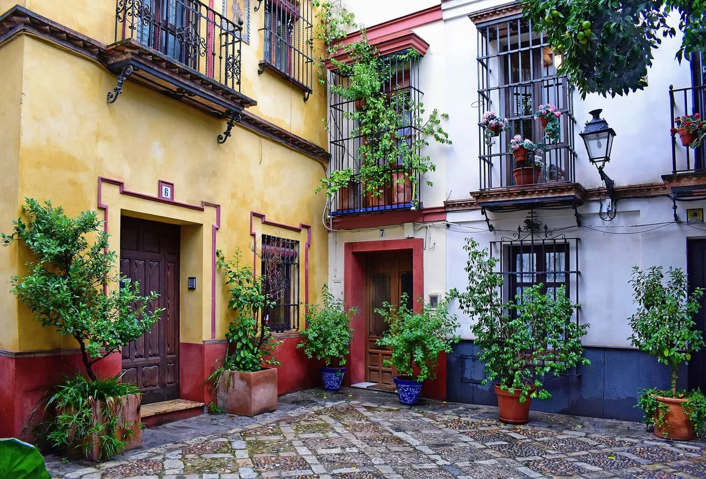 A small cobbled corner in Santa Cruz with an ochre house and a white house, wrought-iron balconies and pots of plants beside the doors