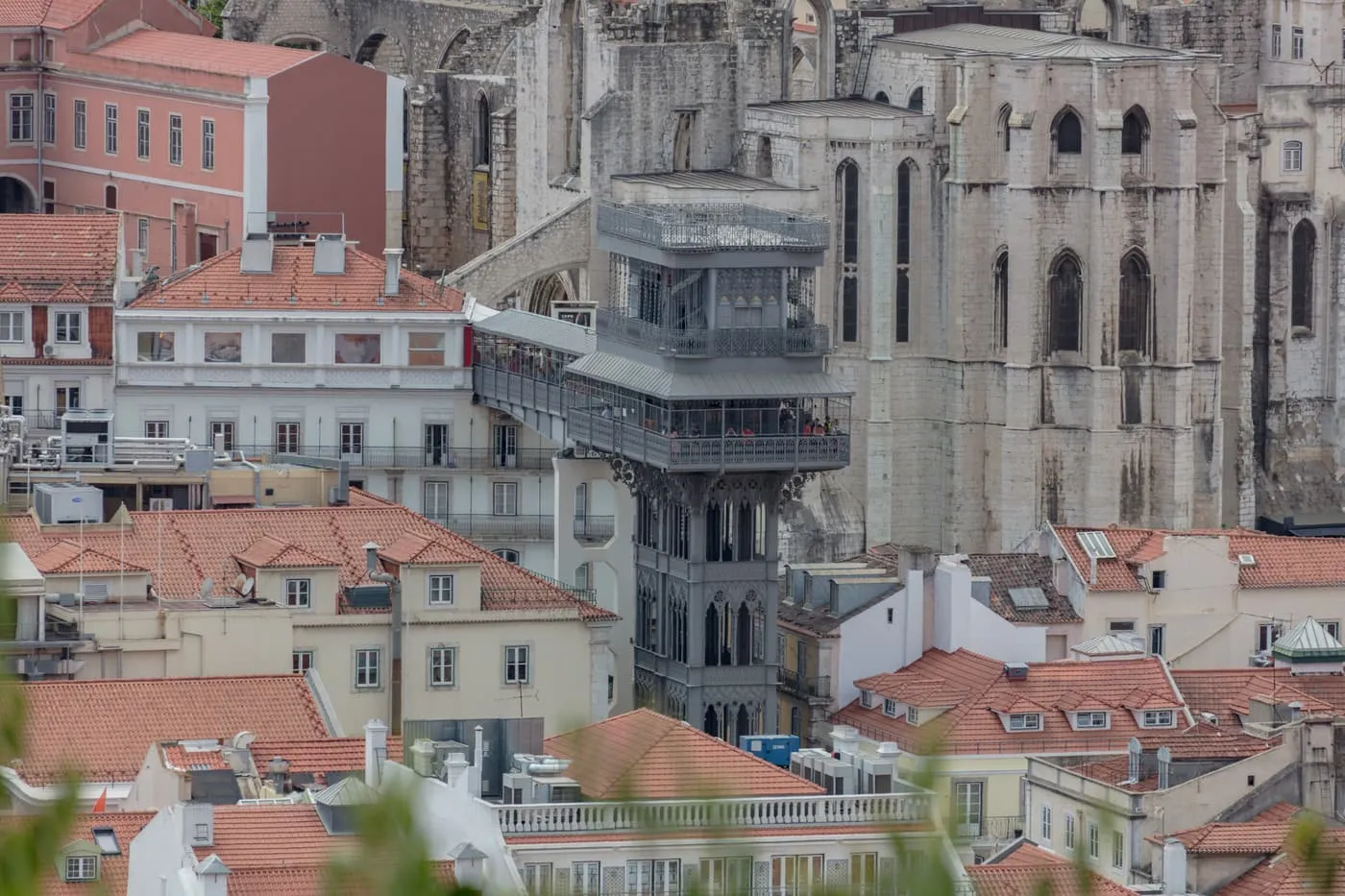 The Santa Justa Lift beside the roofless arches of the Carmo Convent, seen from above across the roofs of the Baixa
