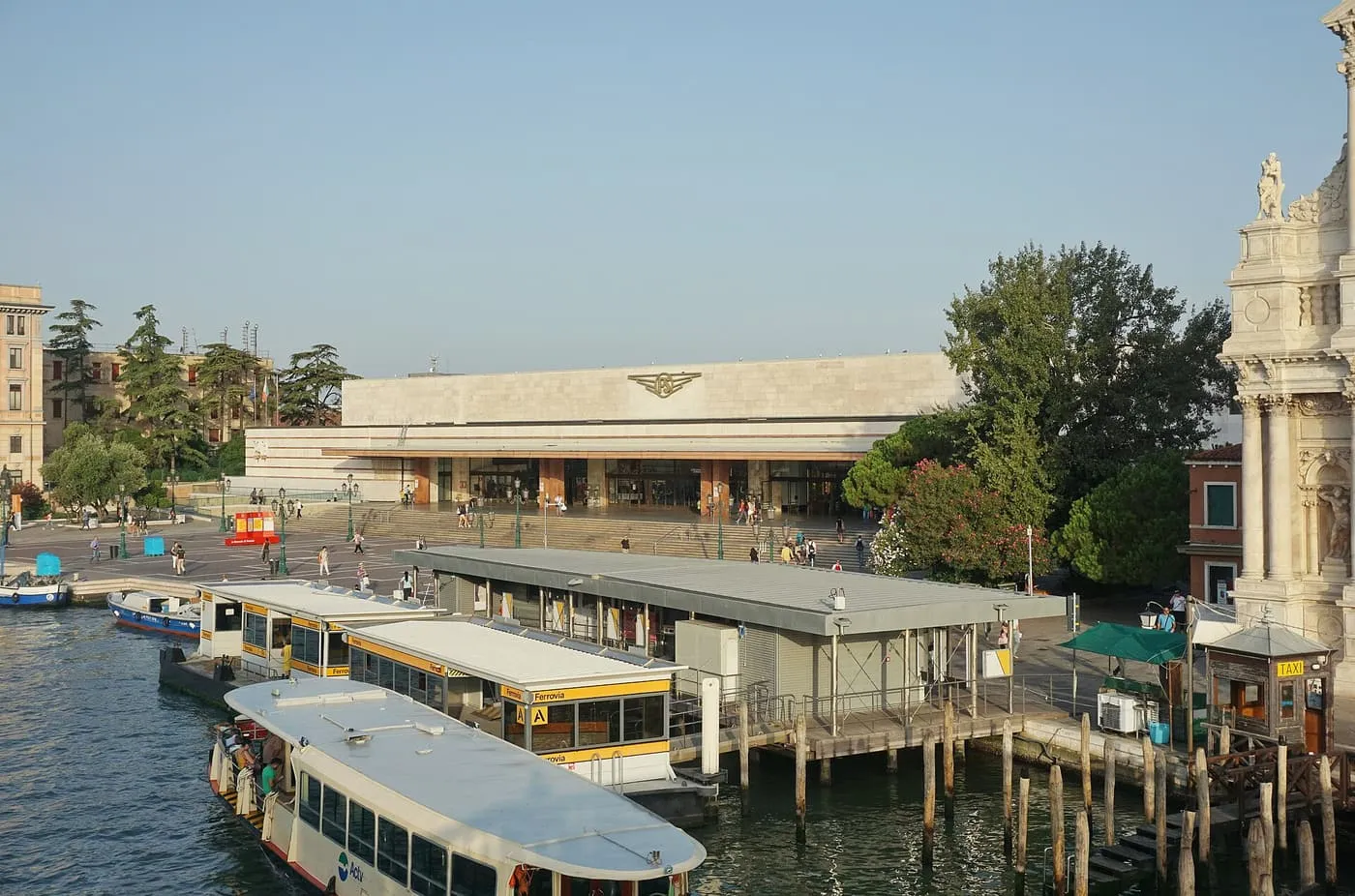 The low stone front of Santa Lucia station across its forecourt, with the Ferrovia vaporetto stop and a vaporetto on the Grand Canal in front