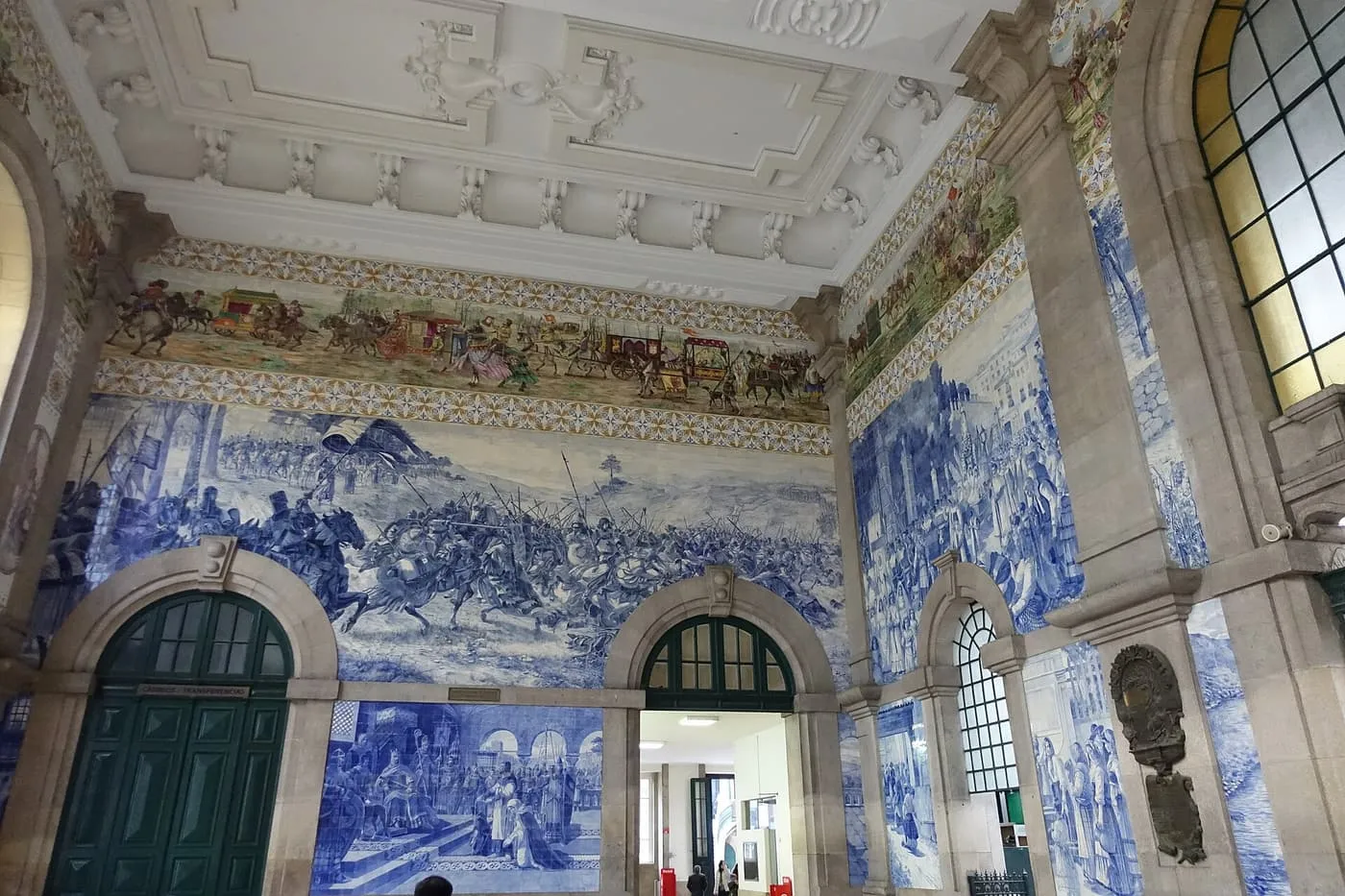 The vestibule of São Bento station, its walls covered in blue-and-white azulejo panels of battles and processions under a white plaster ceiling