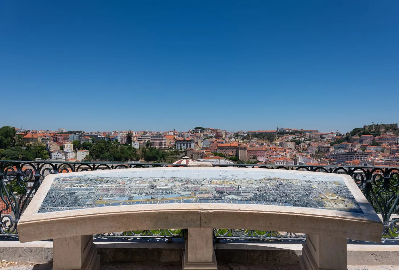 A stone table with a tile map of the city on the viewpoint's balustrade, and the roofs of the Baixa and the castle hill beyond under a blue sky