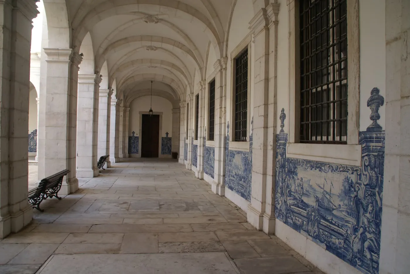 A vaulted cloister gallery with blue and white tile panels along the wall and a bench by the window