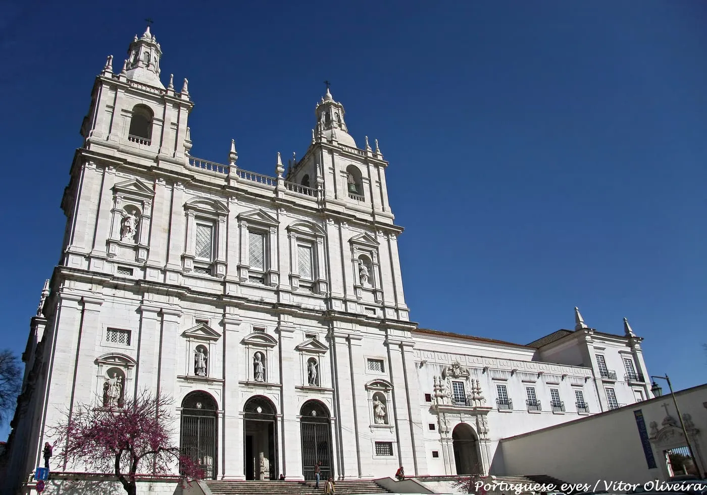 The white Mannerist front of São Vicente de Fora, with two towers, rows of windows and niches, seen from below against a blue sky