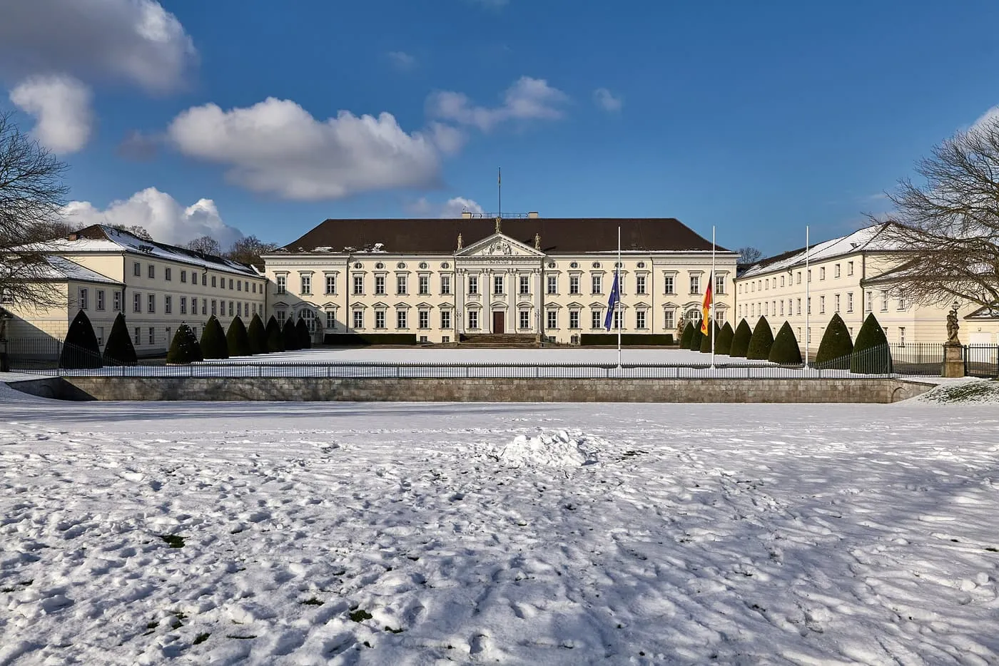 The pale yellow facade of Schloss Bellevue across a snow-covered lawn under a blue sky
