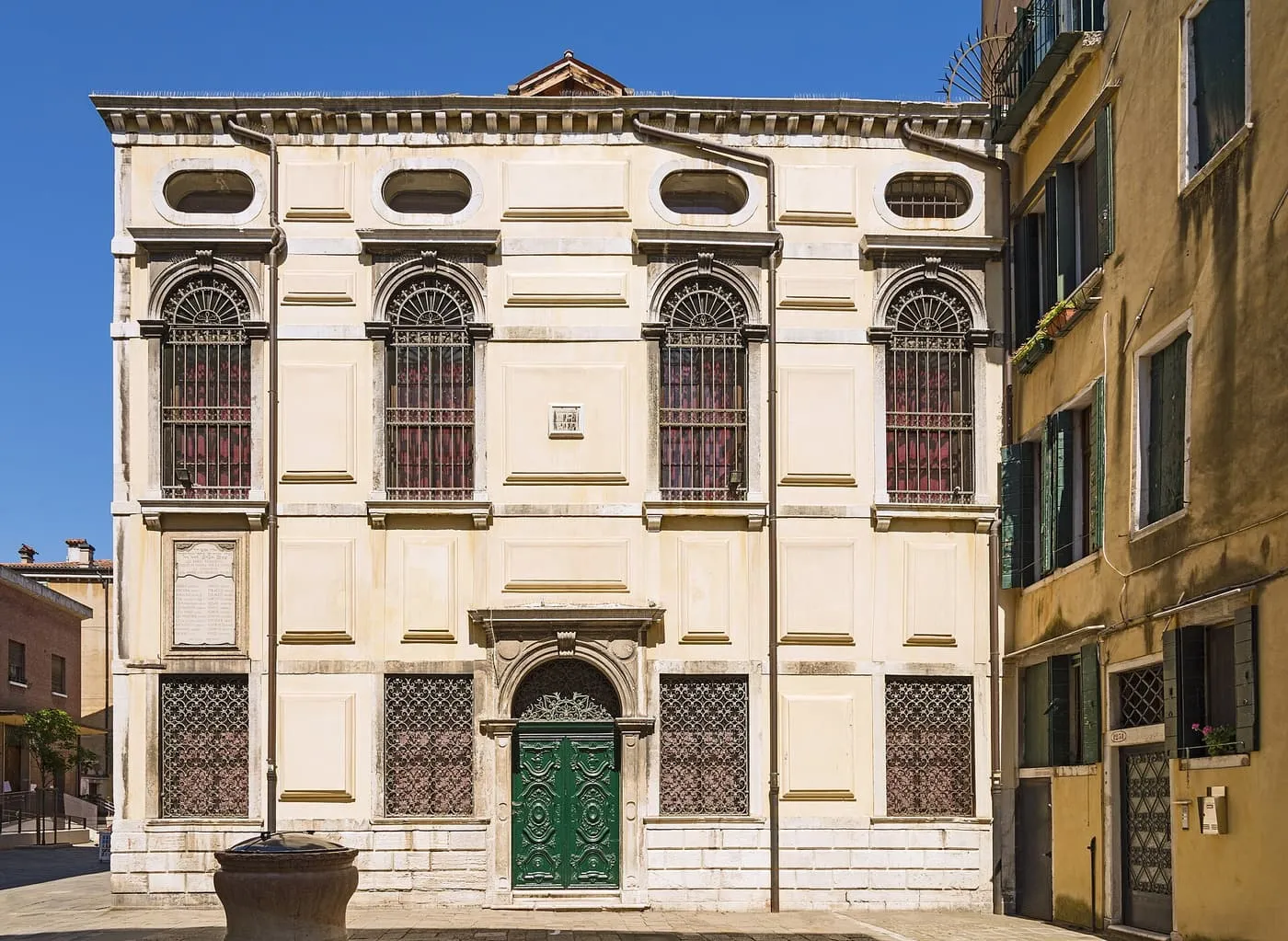 The cream front of the Levantine Synagogue, with arched barred windows and a green door