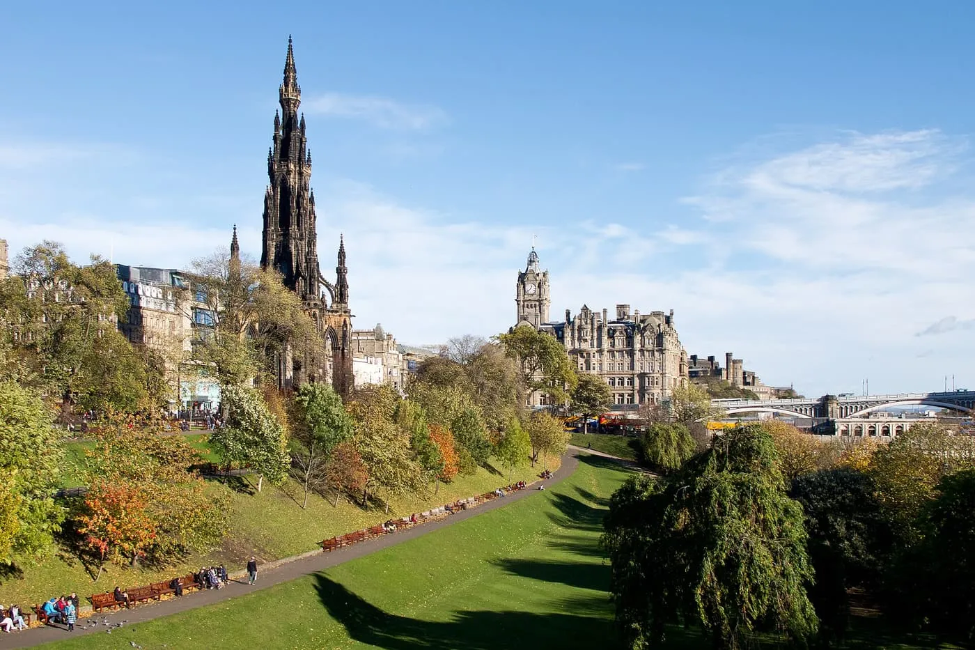 The Gothic spire of the Scott Monument above the trees and paths of Princes Street Gardens, with a clock tower to the right