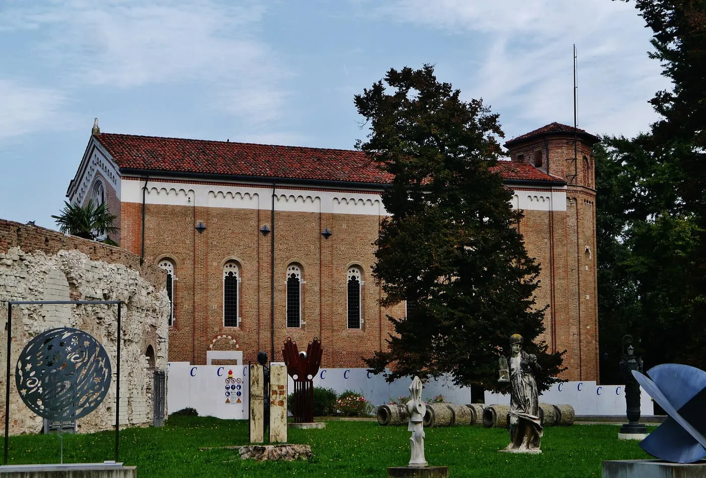 The plain brick south side of the Scrovegni Chapel, with tall narrow windows and a bell tower, seen across a lawn