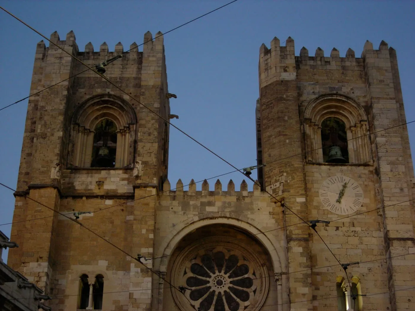 The Sé's two crenellated towers and the rose window between them, seen from the street below with tram cables in front