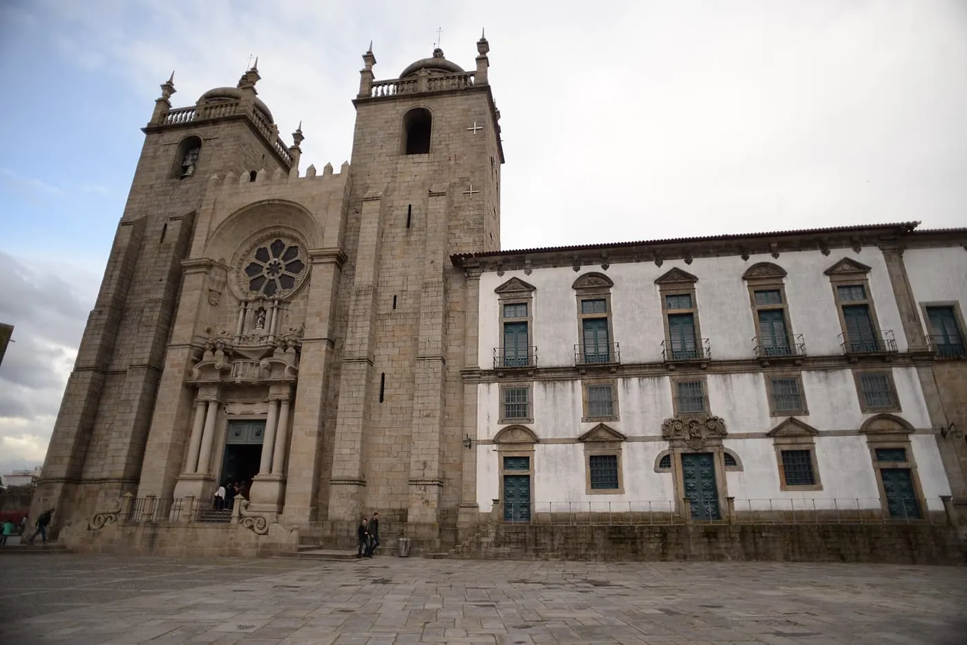 The twin-towered granite west front of Porto Cathedral with a rose window, beside the white bishop's palace across the square