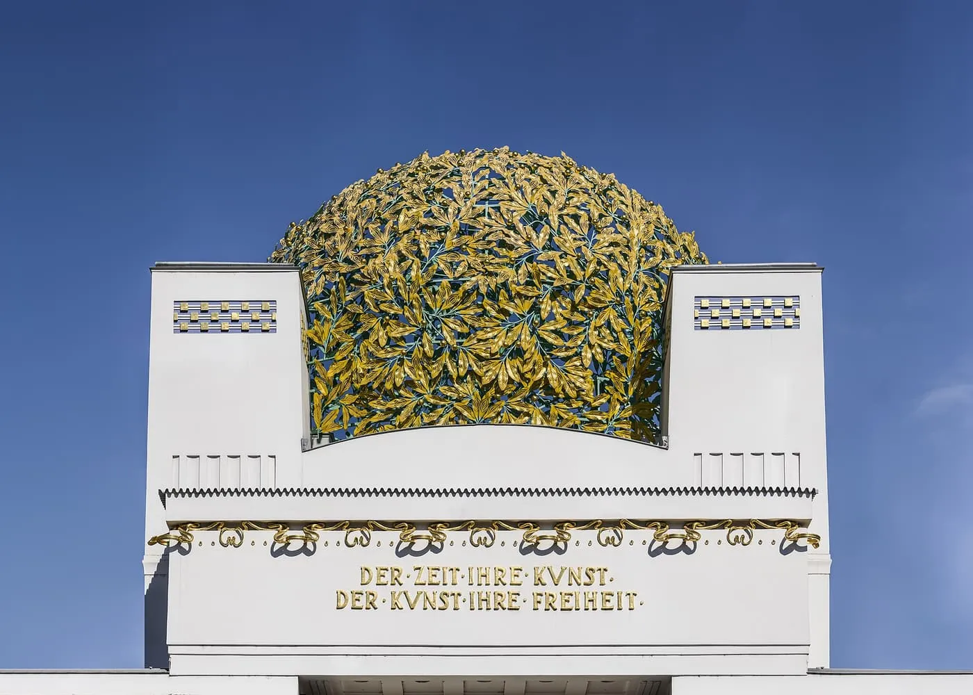 The gilded laurel-leaf dome of the Secession building above a white wall with a gold inscription