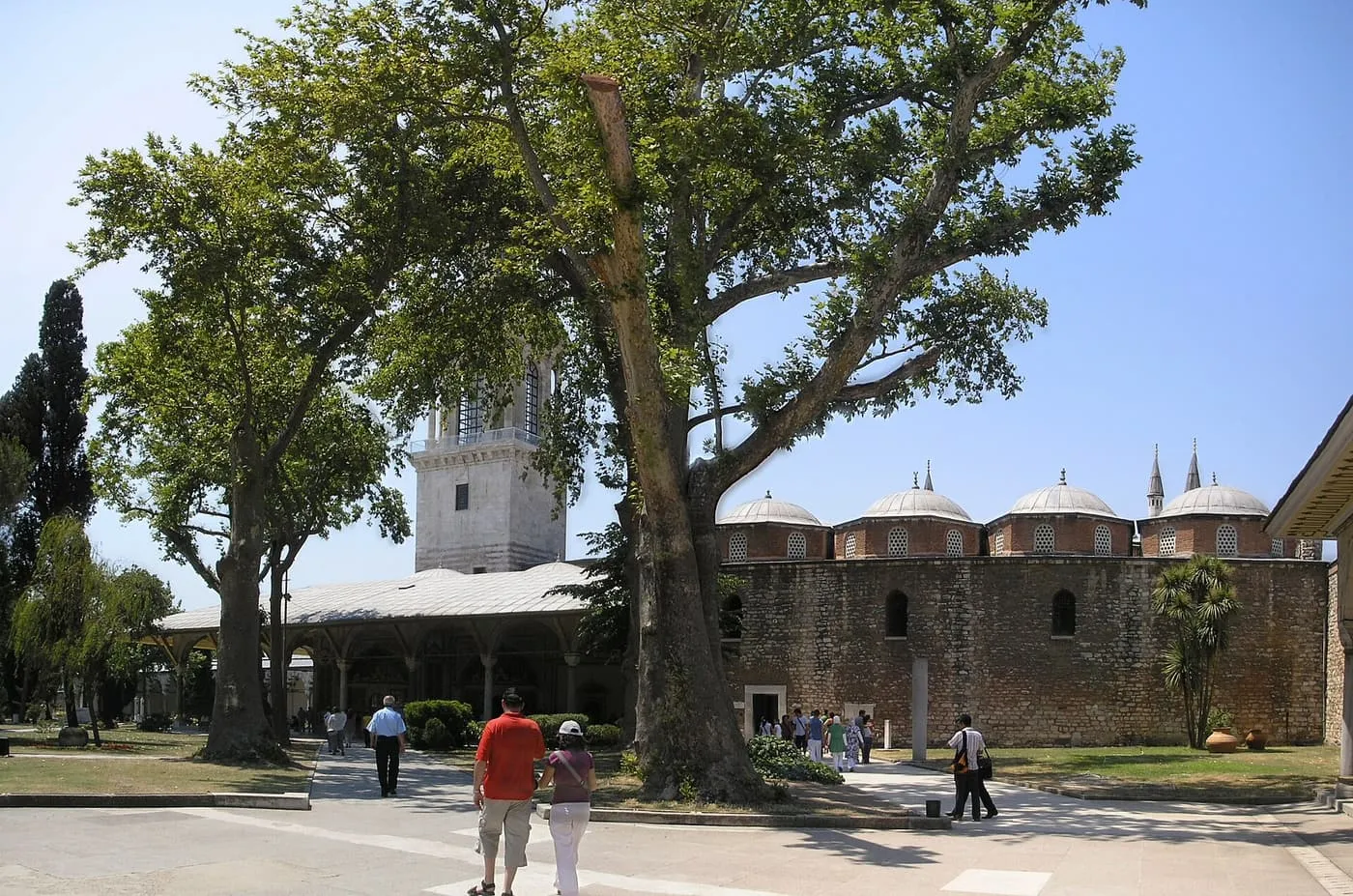 The Tower of Justice rising behind a covered porch in the second court, with a row of domed buildings to the right and a tall plane tree in front