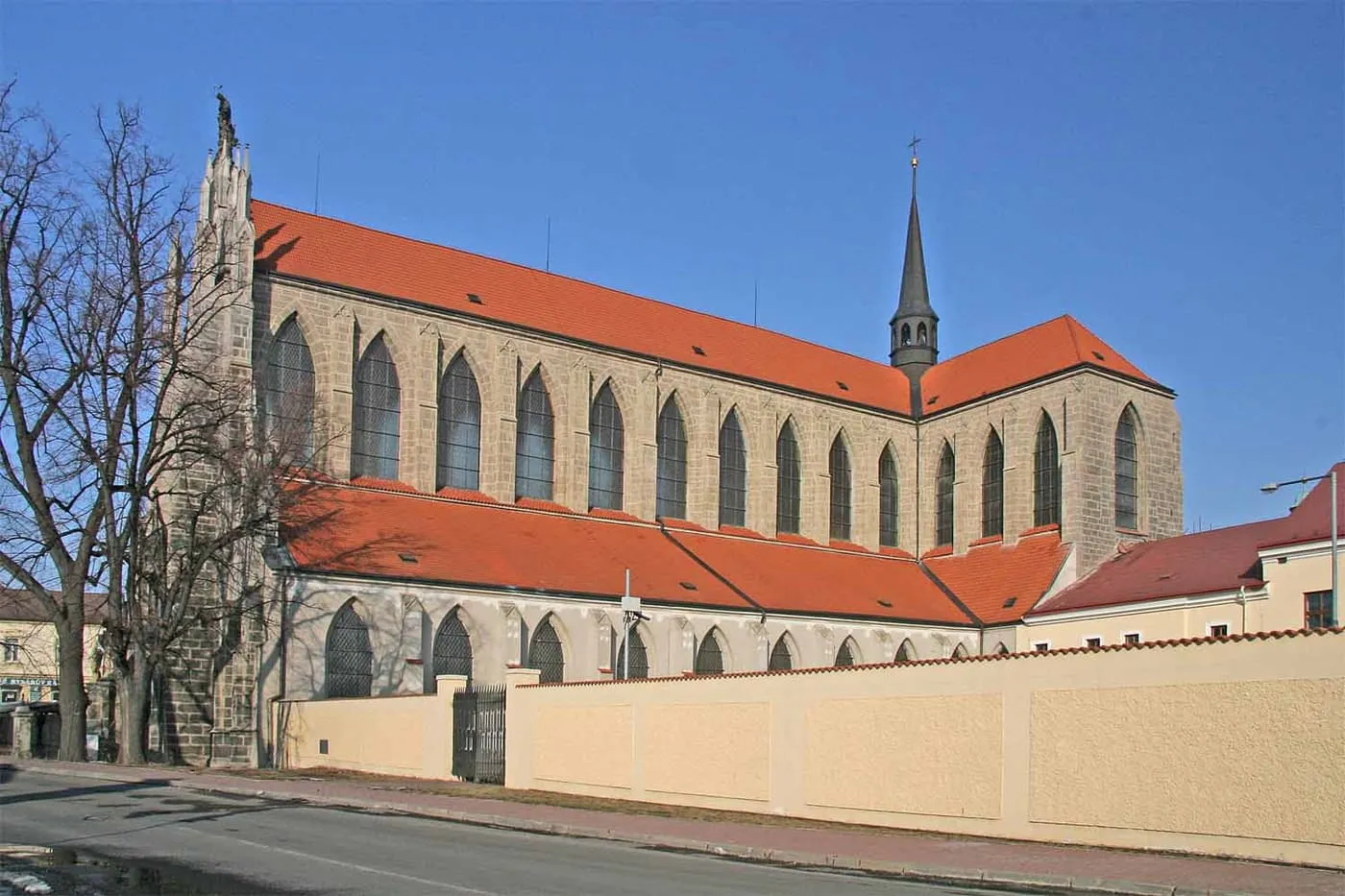 The long side of the Gothic Cathedral of the Assumption of Our Lady at Sedlec, with tall arched windows and a steep red roof, seen from the street