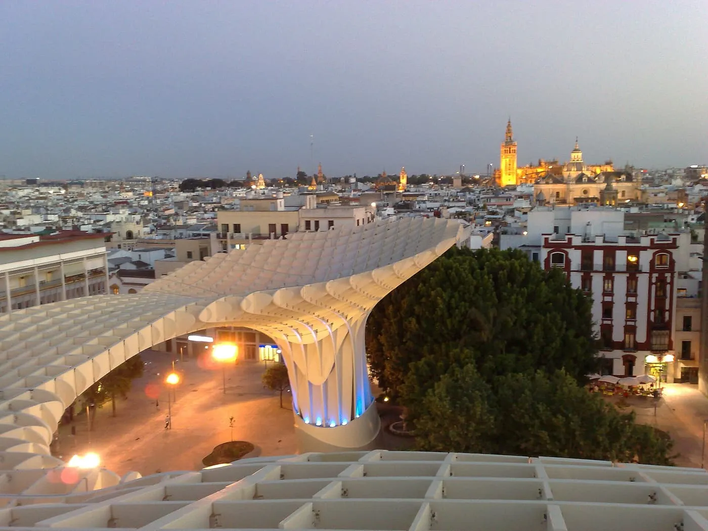 The Metropol Parasol's wooden canopy at dusk seen from its roof, with the lit Cathedral and Giralda on the skyline beyond